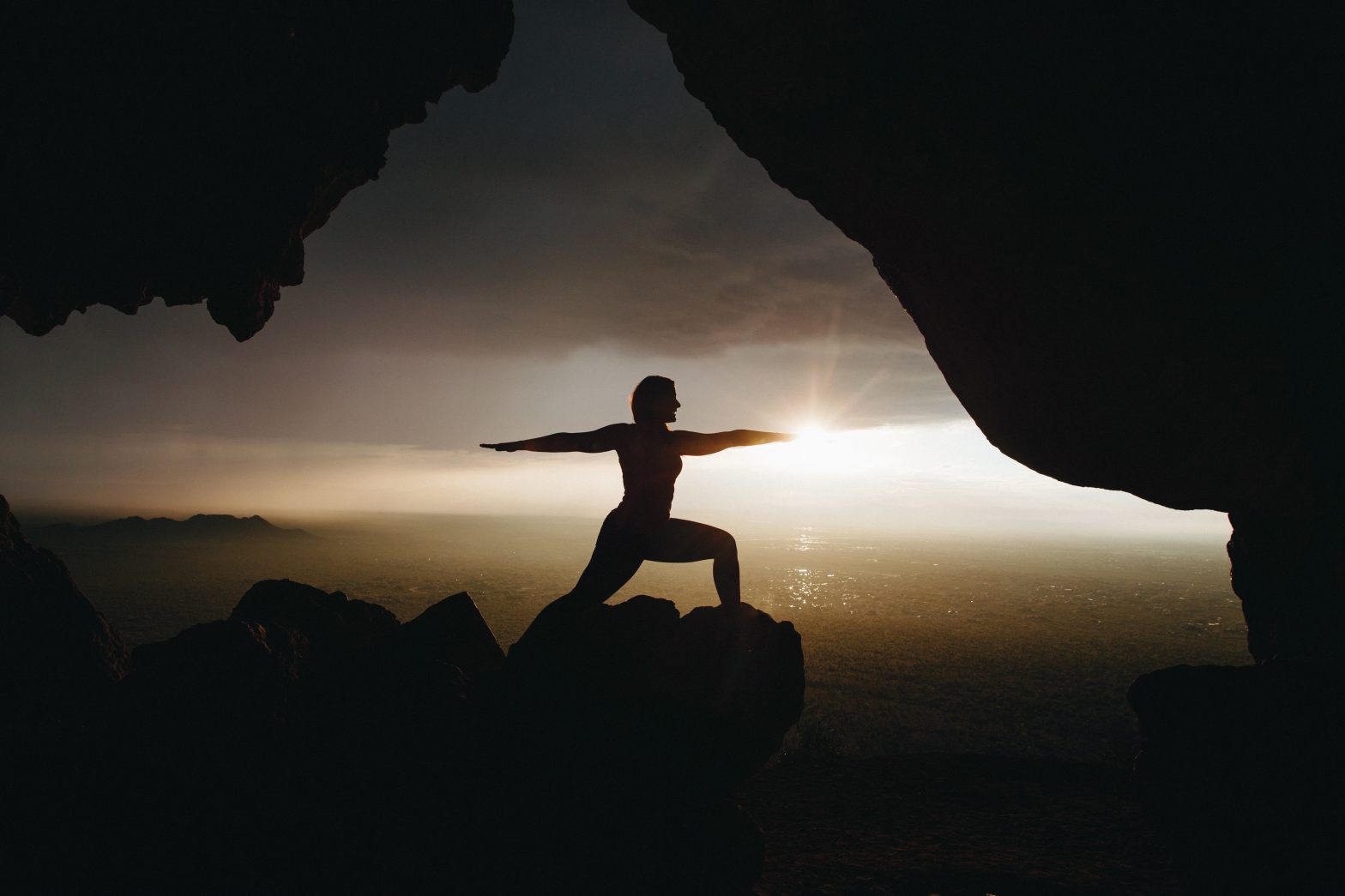 Standing on a rock doing yoga, a woman's silhouette shows that fifteen minutes of daily yoga can boost wellness.